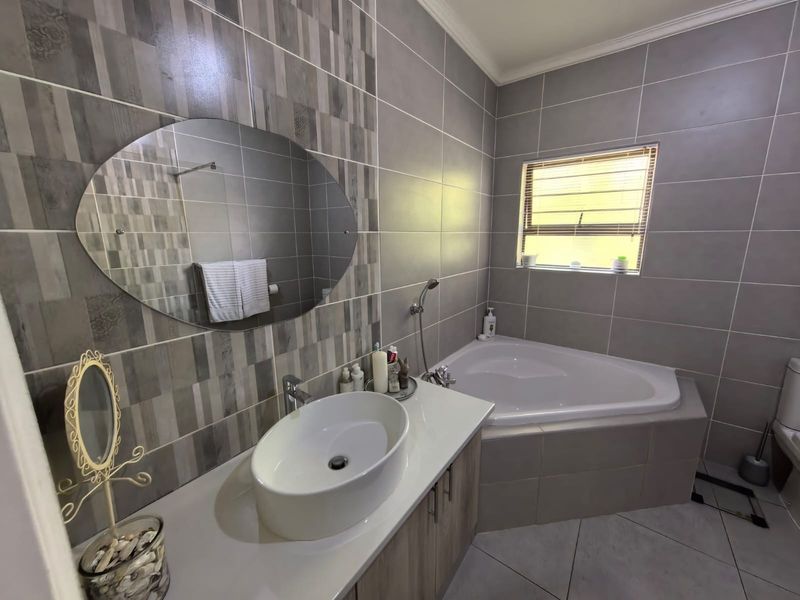 Modern bathroom featuring a corner bathtub, vessel sink vanity with storage, and contemporary grey wall tiling.