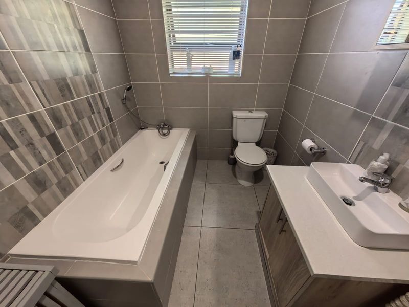 Modern bathroom featuring a built-in bathtub, a vessel sink vanity, and neutral grey floor-to-ceiling tiling.