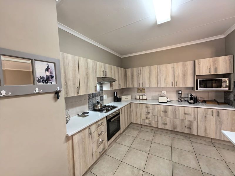 Modern kitchen featuring light wood-grain cabinetry, gas hob, built-in oven, integrated microwave, and neutral tiled flooring.