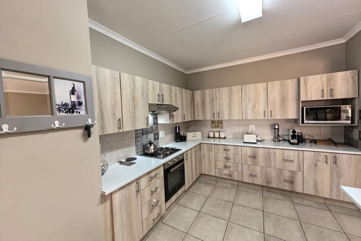 Modern kitchen featuring light wood-grain cabinetry, gas hob, built-in oven, integrated microwave, and neutral tiled flooring.