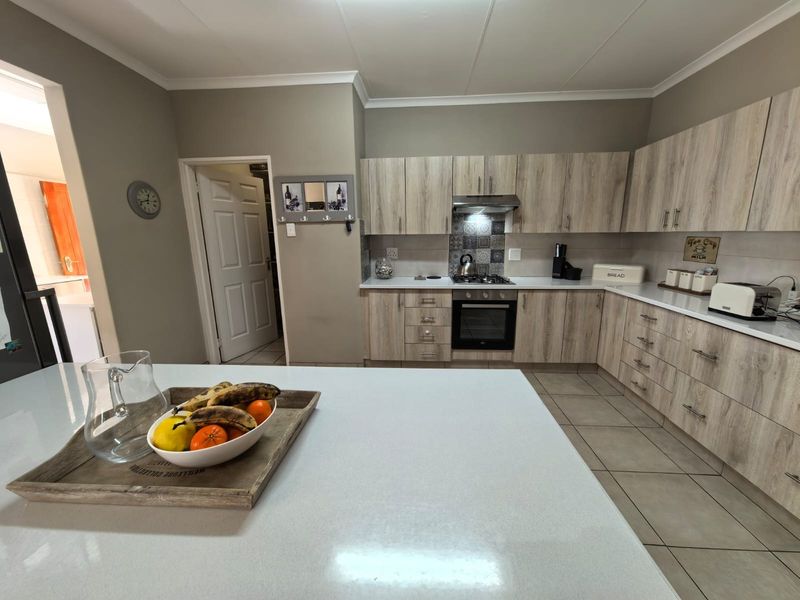 Modern kitchen featuring light wood-grain cabinetry, stone countertops, a central island, and integrated stainless steel appliances with a decorative tiled backsplash.