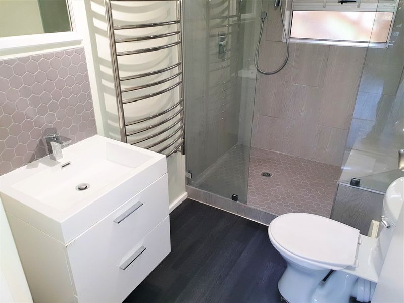 Modern bathroom featuring a sleek vanity, walk-in shower with glass enclosure, and a wall-mounted heated towel rail.