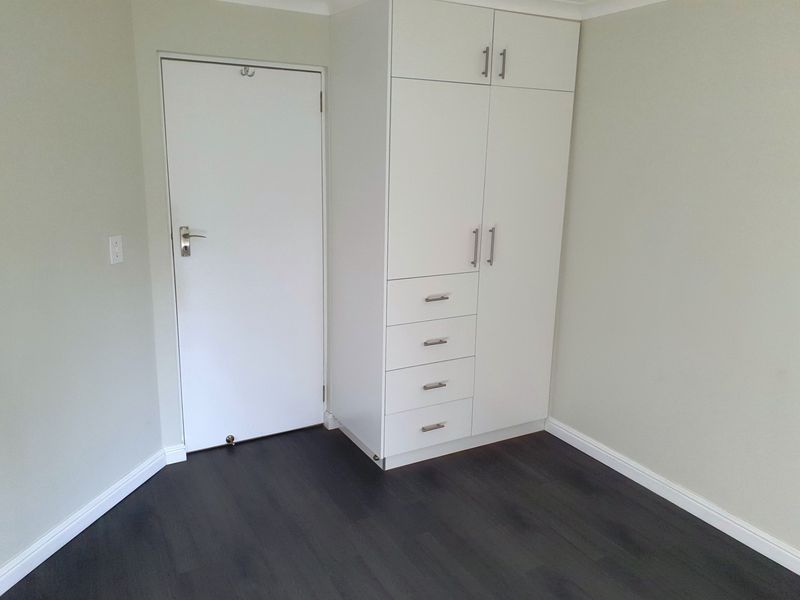A clean, empty bedroom featuring dark laminate flooring, neutral walls, and a white built-in wardrobe with integrated drawers.