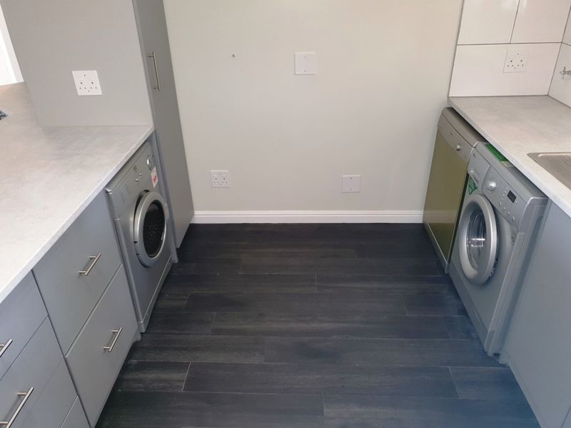 A functional laundry area featuring modern grey cabinetry, laminate countertops, and integrated appliances with dark wood-look laminate flooring.
