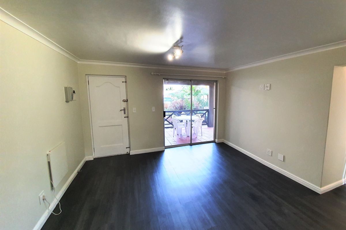 A bright, empty living room featuring dark laminate flooring, cove cornicing, and a sliding glass door providing access to an outdoor patio area.