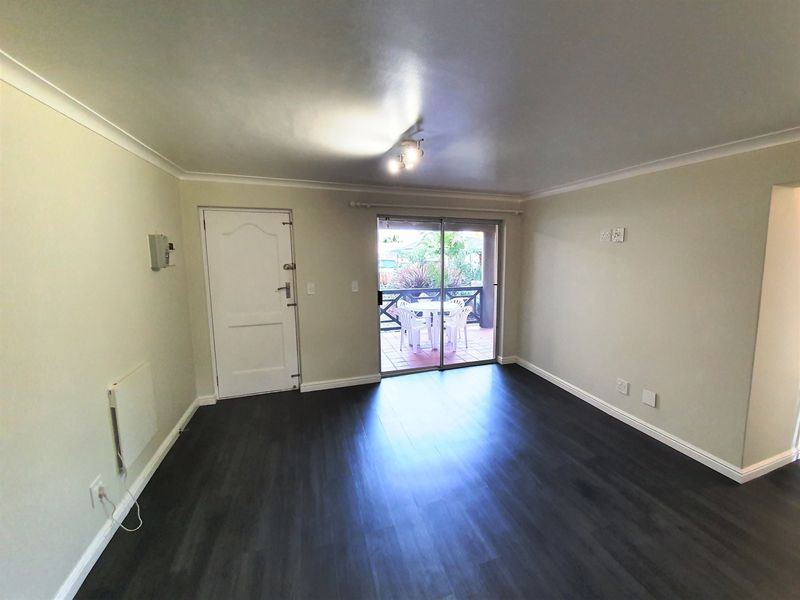 A bright, empty living room featuring dark laminate flooring, cove cornicing, and a sliding glass door providing access to an outdoor patio area.