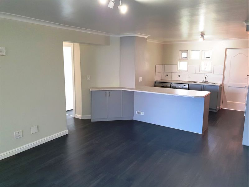 An open-plan living and kitchen area featuring dark laminate flooring, neutral walls, and a functional kitchen layout with a breakfast bar.
