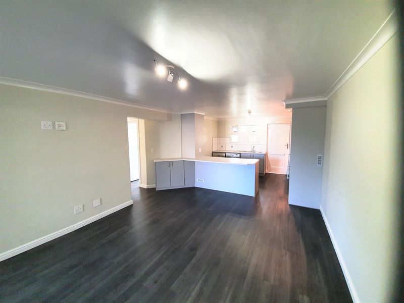 An open-plan living and kitchen area featuring dark laminate flooring, neutral walls, and a functional kitchen layout with built-in cabinetry and counter space.