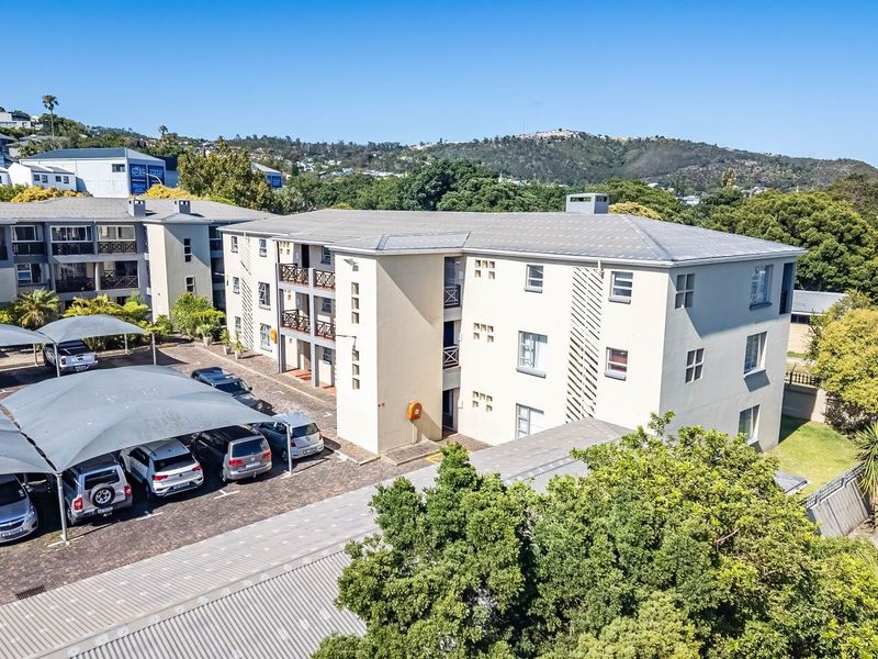 Aerial view of a multi-story apartment complex featuring a paved parking area with shade sails and established surrounding greenery.