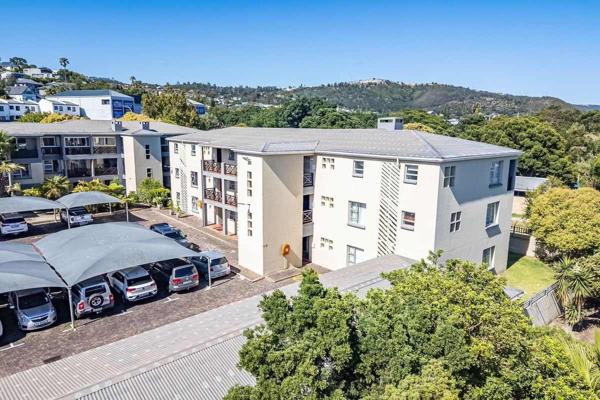 Aerial view of a multi-story apartment complex featuring a paved parking area with shade sails and established surrounding greenery.