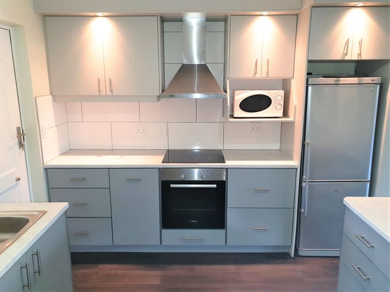Modern kitchen featuring grey cabinetry, stainless steel appliances including an oven and extractor fan, tiled backsplash, and integrated lighting.