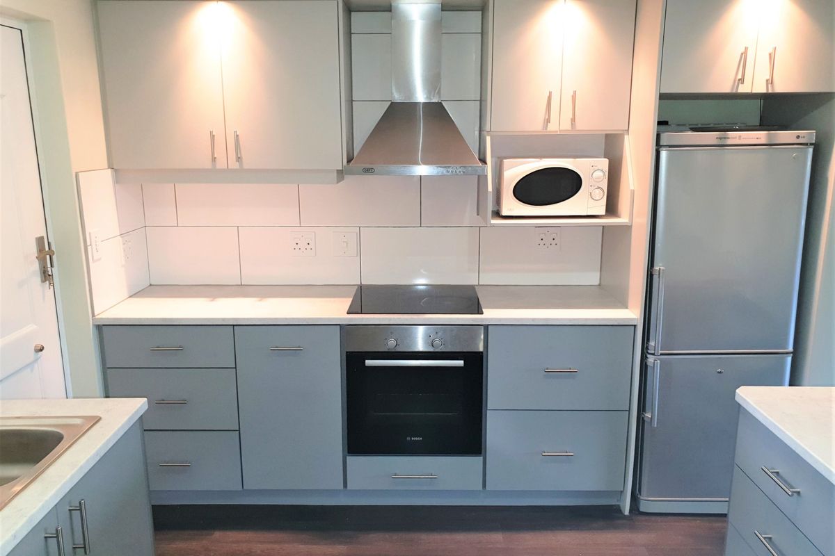 Modern kitchen featuring grey cabinetry, stainless steel appliances including an oven and extractor fan, tiled backsplash, and integrated lighting.