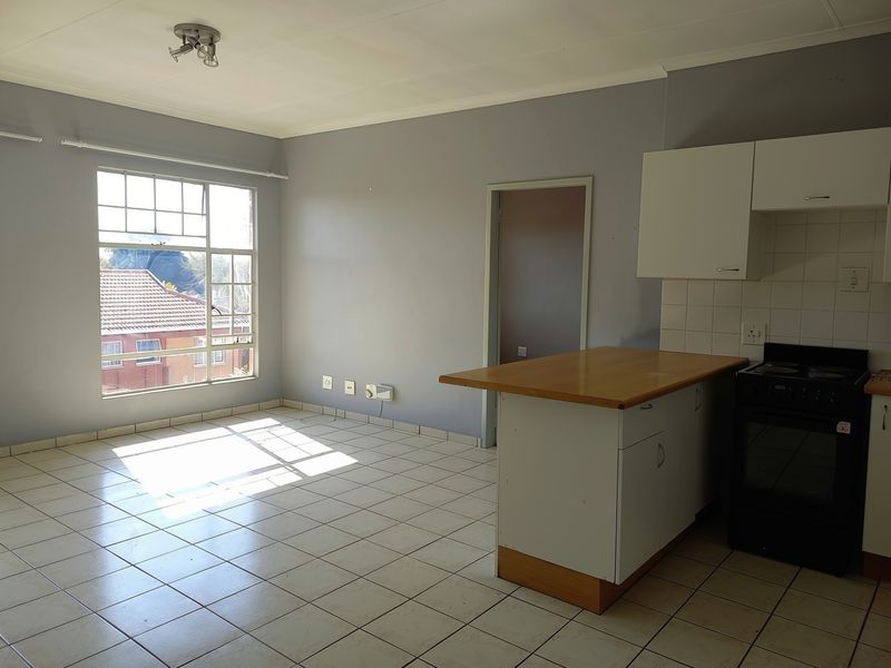 Open-plan living and kitchen area featuring tiled flooring, built-in cabinetry, and a breakfast counter, offering a functional and bright space.