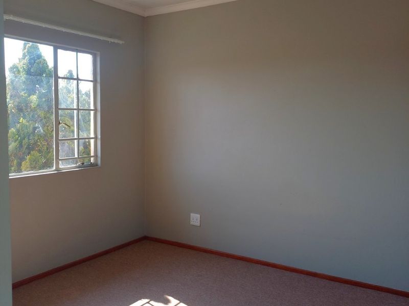 A bright, empty bedroom featuring neutral wall paint, carpeted flooring, and a window that allows for natural light.