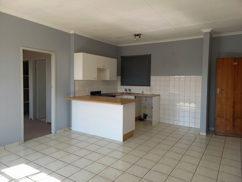 An empty kitchen featuring tiled flooring, a laminate countertop, built-in cabinetry, and a tiled backsplash, requiring some maintenance and cosmetic updates.