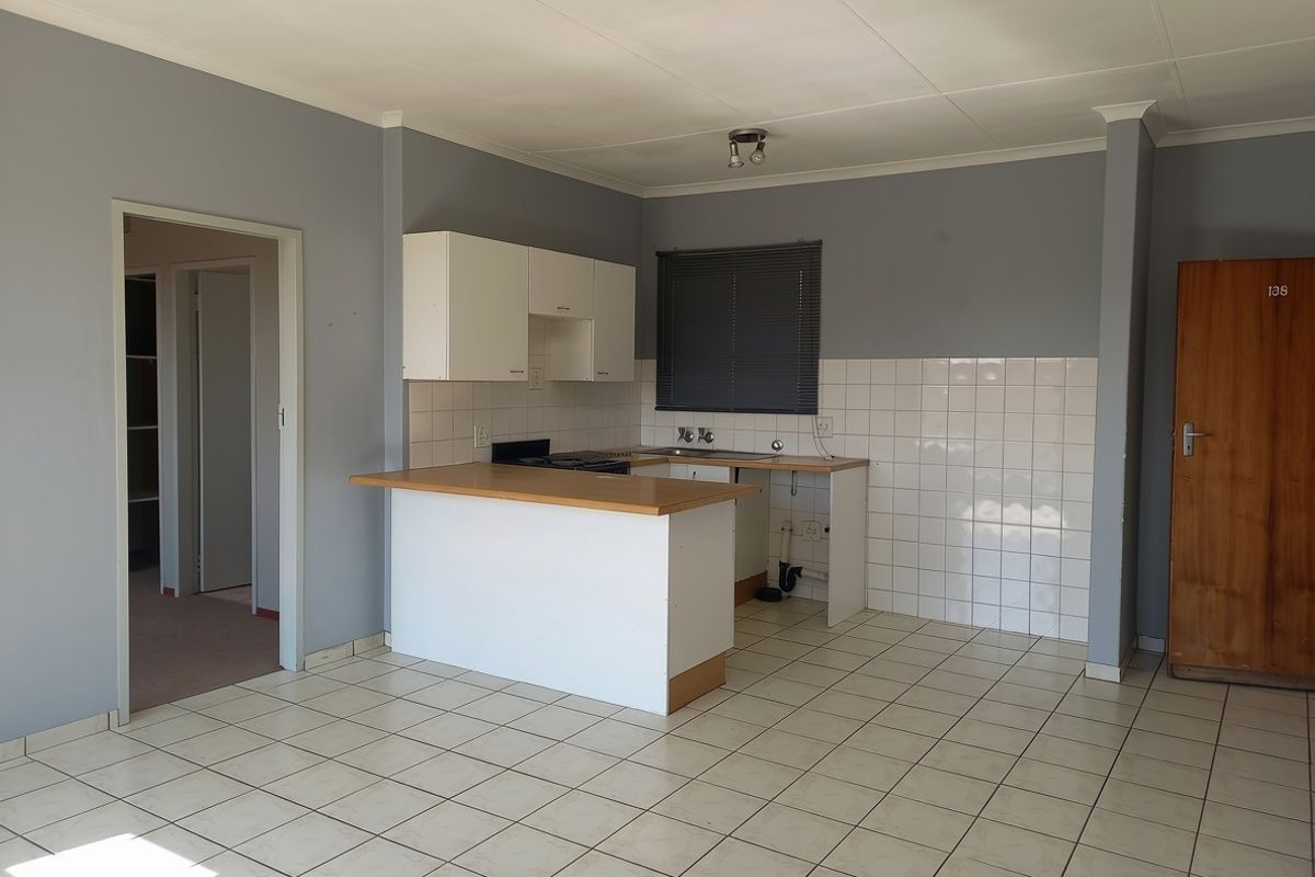 An empty kitchen featuring tiled flooring, a laminate countertop, built-in cabinetry, and a tiled backsplash, requiring some maintenance and cosmetic updates.