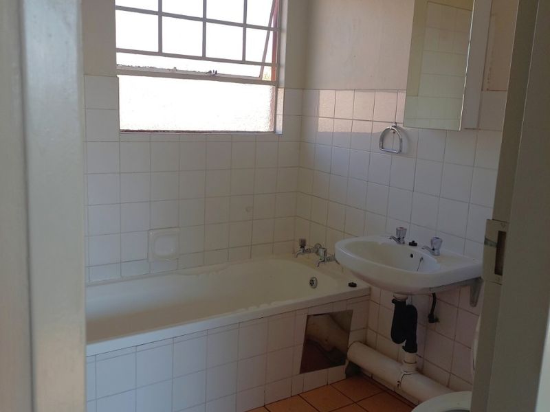 A dated bathroom featuring a bathtub, pedestal basin, and toilet with tiled finishes, requiring cosmetic updates and minor repairs to the bathtub apron.