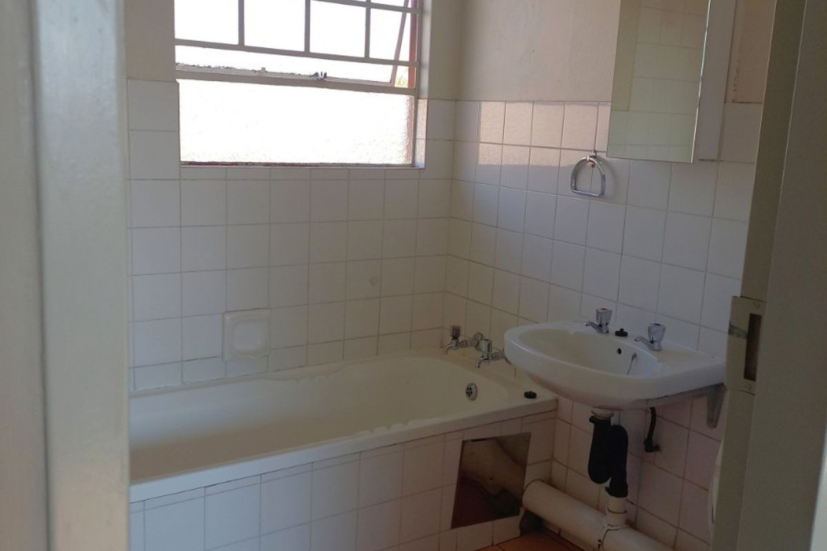 A dated bathroom featuring a bathtub, pedestal basin, and toilet with tiled finishes, requiring cosmetic updates and minor repairs to the bathtub apron.