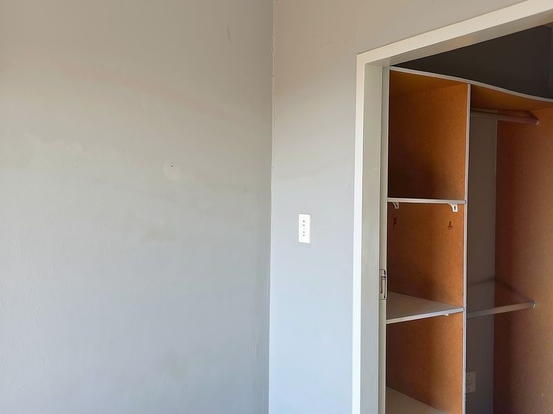 A bedroom interior featuring a built-in wardrobe with shelving and hanging space, showing signs of wear on the wall surfaces.
