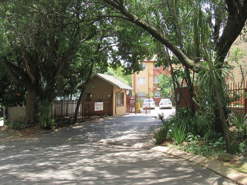Entrance view of the apartment complex featuring a security gate, guard house, and paved driveway access.