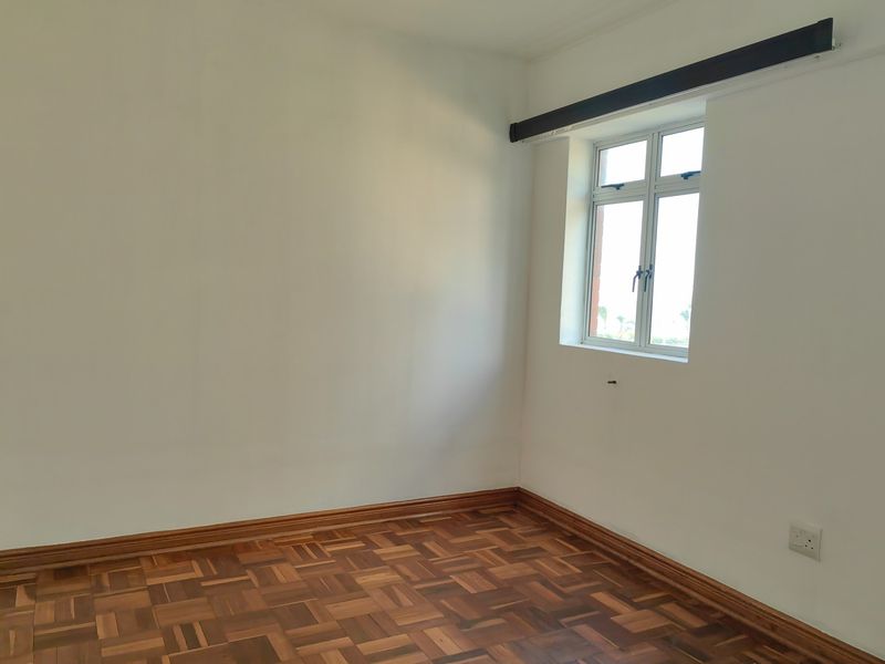 A bright, empty bedroom featuring classic parquet flooring, timber skirting boards, and a casement window, offering a clean canvas for personalization.