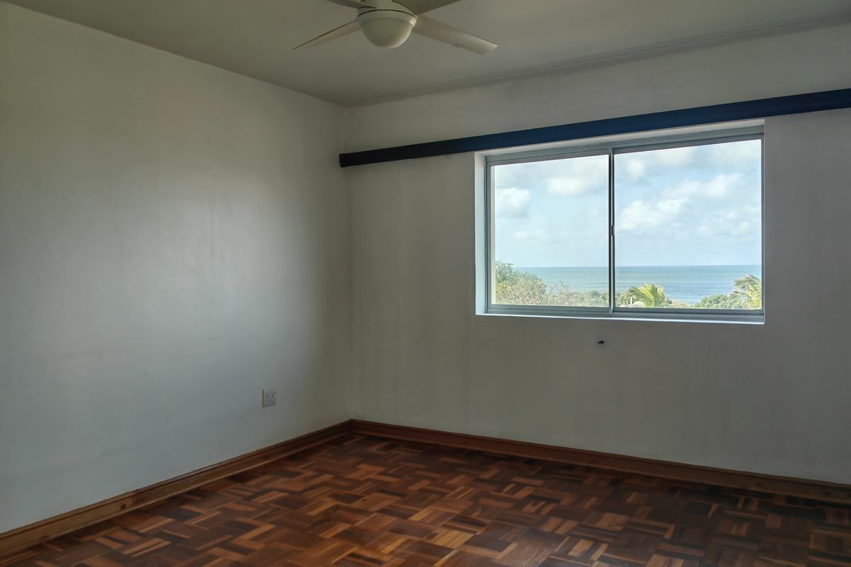 An empty bedroom featuring classic parquet flooring, a ceiling fan, and a window offering a scenic ocean view.