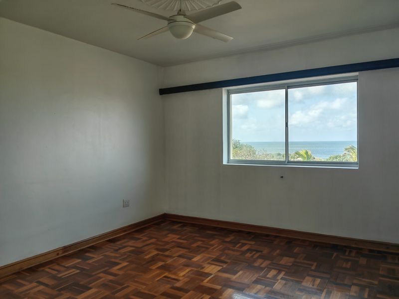 An empty bedroom featuring classic parquet flooring, a ceiling fan, and a window offering a scenic ocean view.