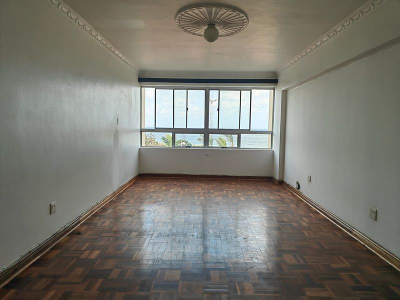 An empty living room featuring original parquet flooring, decorative ceiling rose, and large windows offering ocean views.