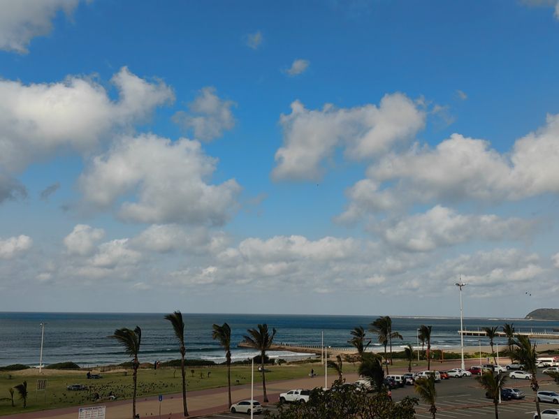 A scenic elevated view overlooking the coastline, beach, and public parking area.