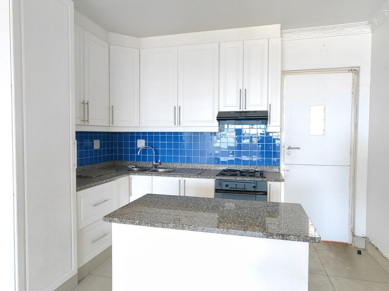 A clean, functional kitchen featuring white cabinetry, granite countertops, a gas hob with extractor, and a vibrant blue tiled backsplash.