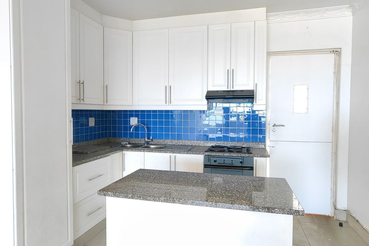 A clean, functional kitchen featuring white cabinetry, granite countertops, a gas hob with extractor, and a vibrant blue tiled backsplash.