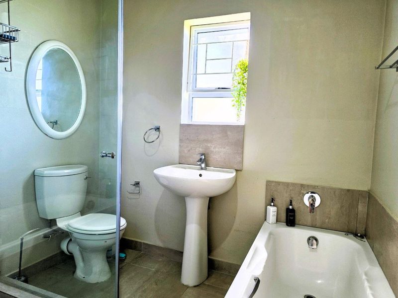 A clean and functional bathroom featuring a pedestal basin, bathtub, and a separate shower area with a glass screen.
