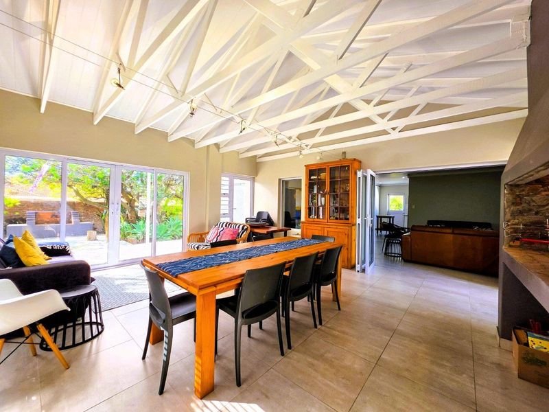 Spacious open-plan living and dining area featuring high exposed timber truss ceilings, large sliding doors to the garden, and a built-in fireplace.