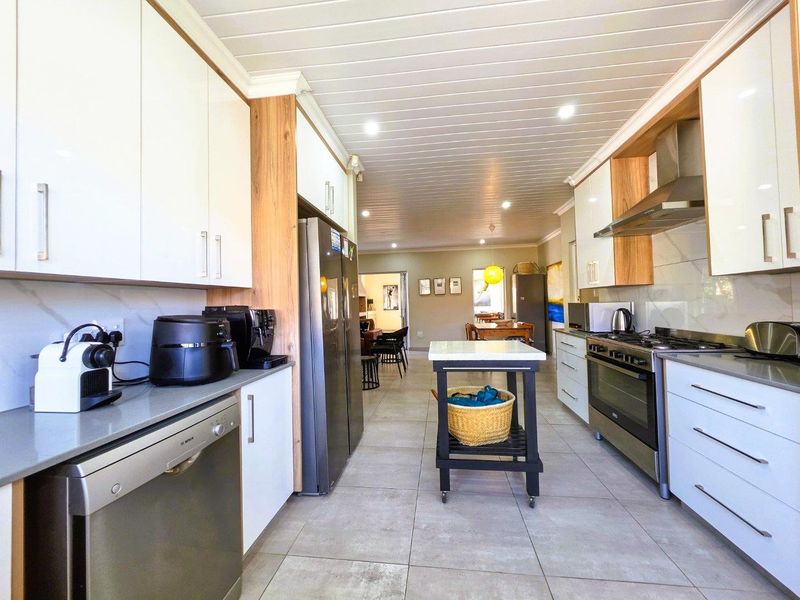 Modern galley-style kitchen featuring sleek white cabinetry, stone countertops, high-end stainless steel appliances, and a clean, contemporary aesthetic with recessed lighting.
