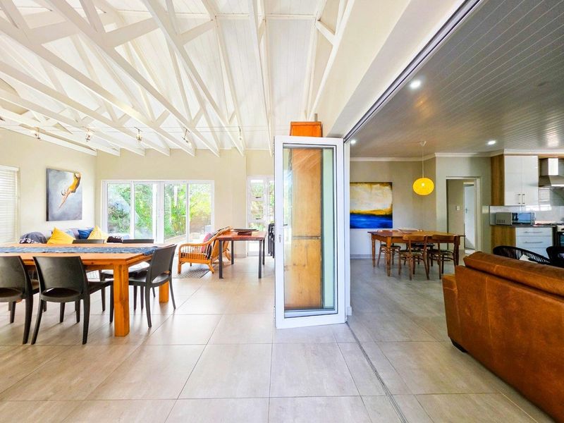 Spacious open-plan living and dining area featuring high vaulted ceilings with exposed trusses, tiled floors, and seamless flow to the kitchen and outdoor space.