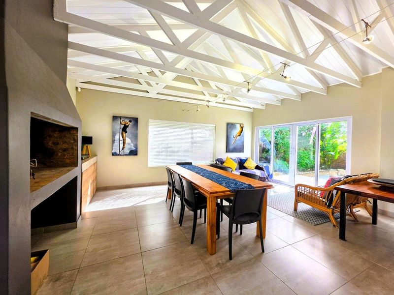 Spacious open-plan living and dining area featuring a striking exposed truss ceiling, built-in fireplace, and large sliding doors opening to the garden.