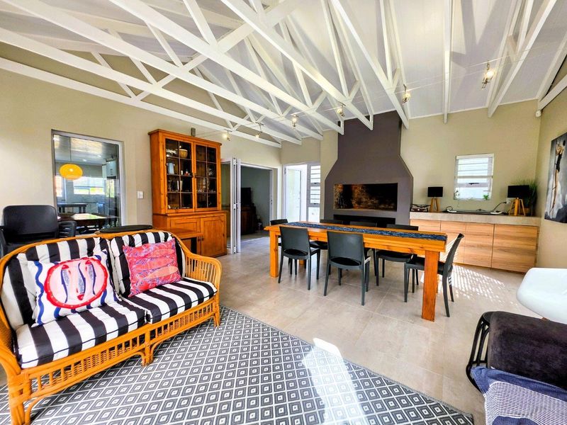 Spacious open-plan living and dining area featuring high exposed timber roof trusses, a large built-in fireplace, and neutral tiled flooring.