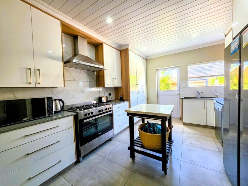 Modern kitchen featuring white cabinetry, stone countertops, gas stove with extractor fan, tiled flooring, and a bright, functional layout with direct outdoor access.