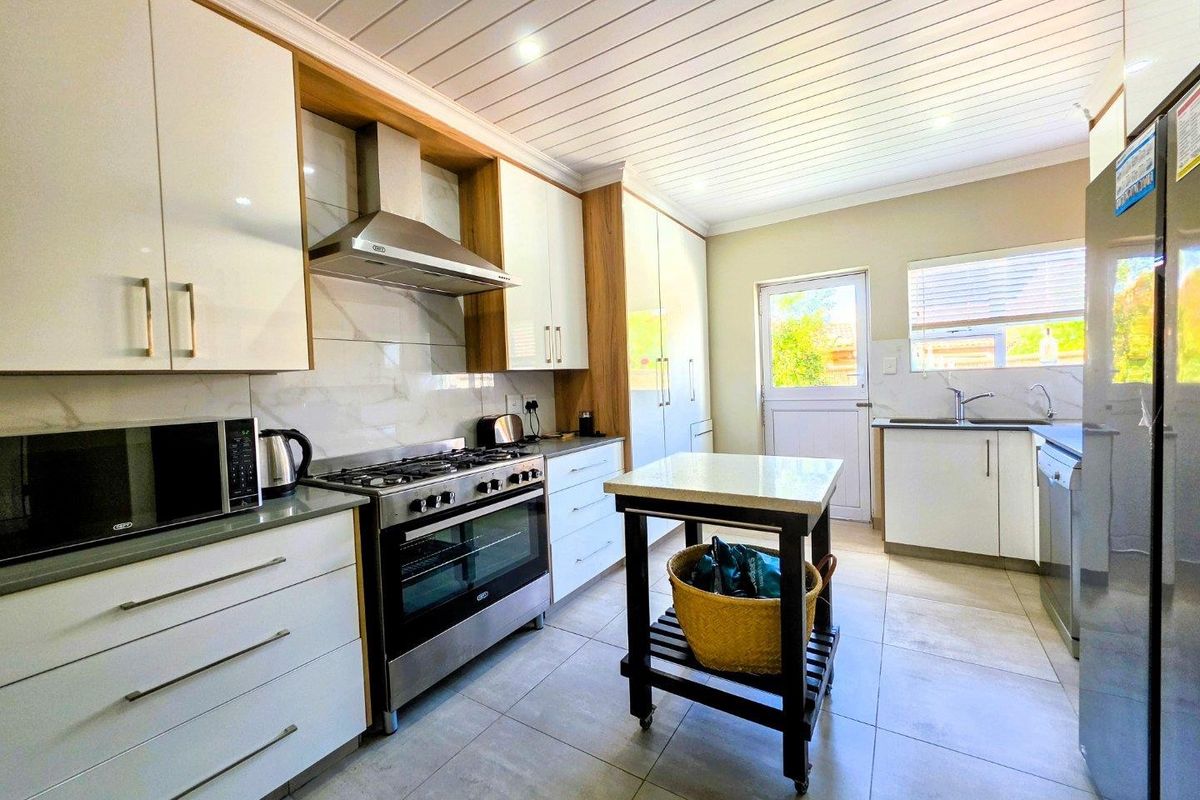 Modern kitchen featuring white cabinetry, stone countertops, gas stove with extractor fan, tiled flooring, and a bright, functional layout with direct outdoor access.