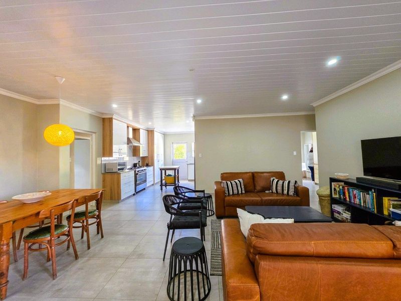 Spacious open-plan living and dining area featuring tiled floors, a modern kitchen with built-in cabinetry, and a distinctive tongue and groove ceiling.