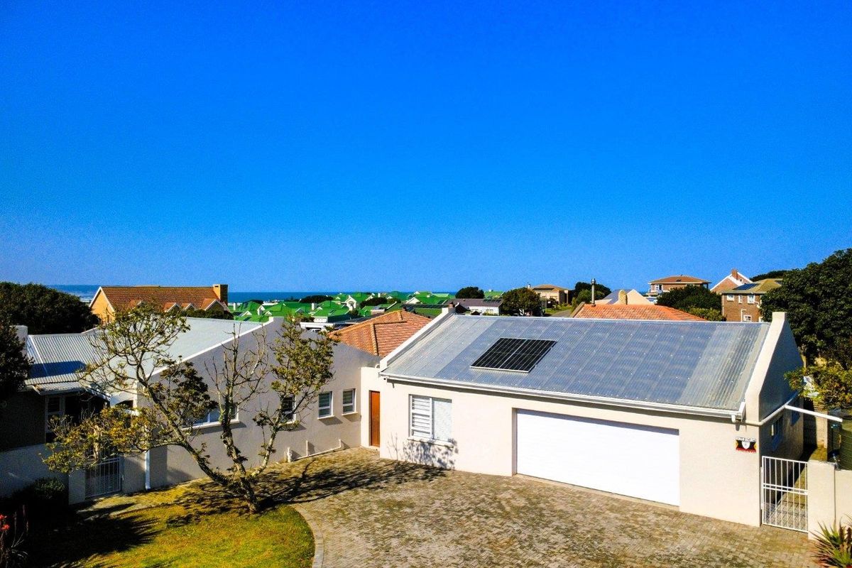 Aerial view of the property featuring a paved driveway, garage, and solar panels on a corrugated metal roof, set within a residential neighborhood.