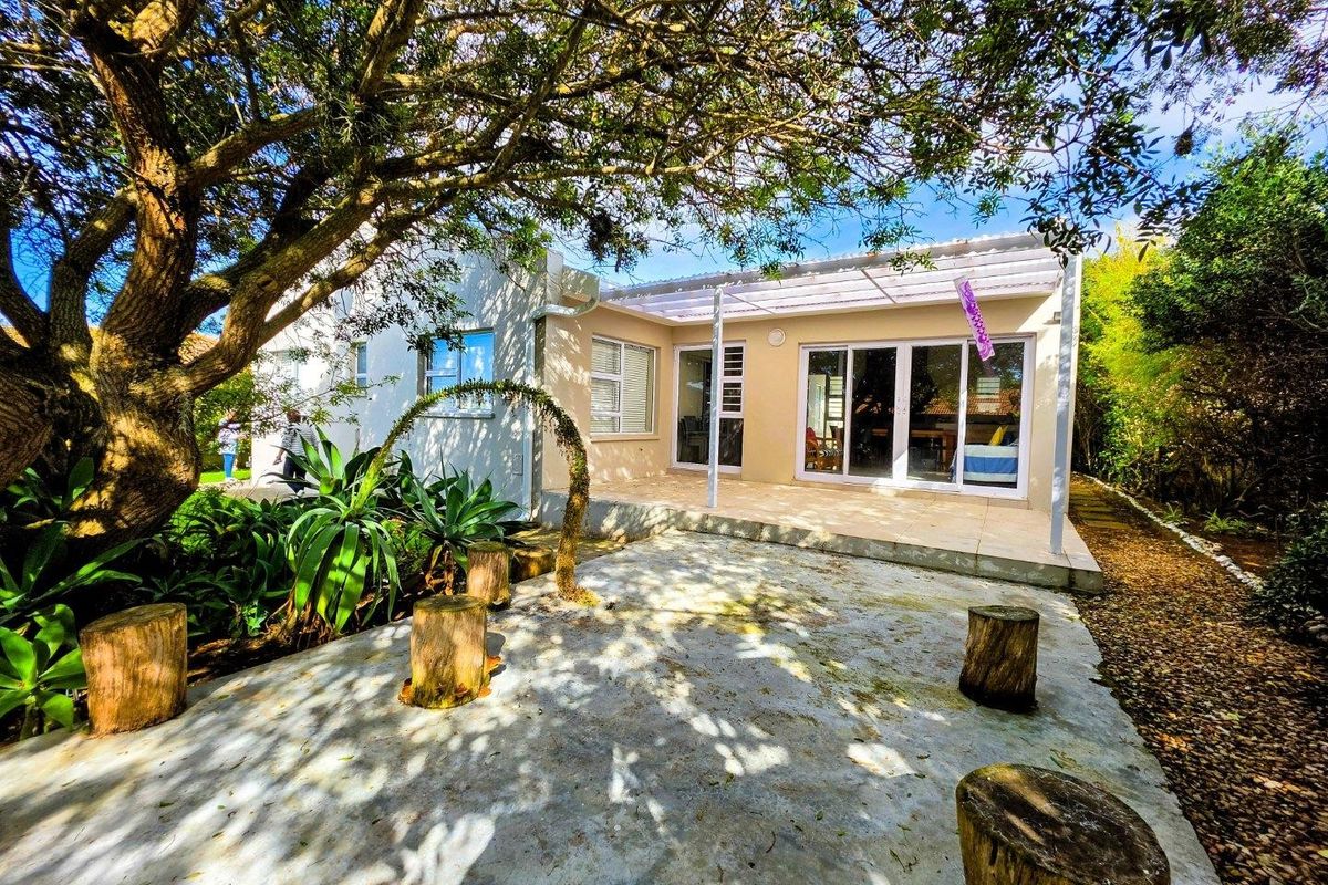 Rear exterior view featuring a covered patio area with tiled flooring, sliding glass doors, and surrounding garden space with mature trees.