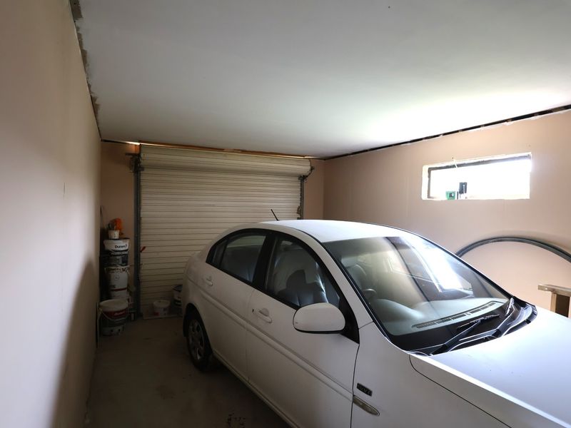 A functional garage space featuring a roller shutter door, concrete flooring, and a small window, currently in need of finishing touches to the ceiling.