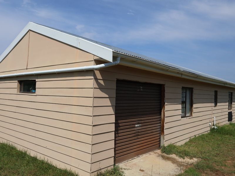 A detached garage structure featuring timber cladding, a corrugated metal roof, and a roller shutter door, set on a grassed plot.