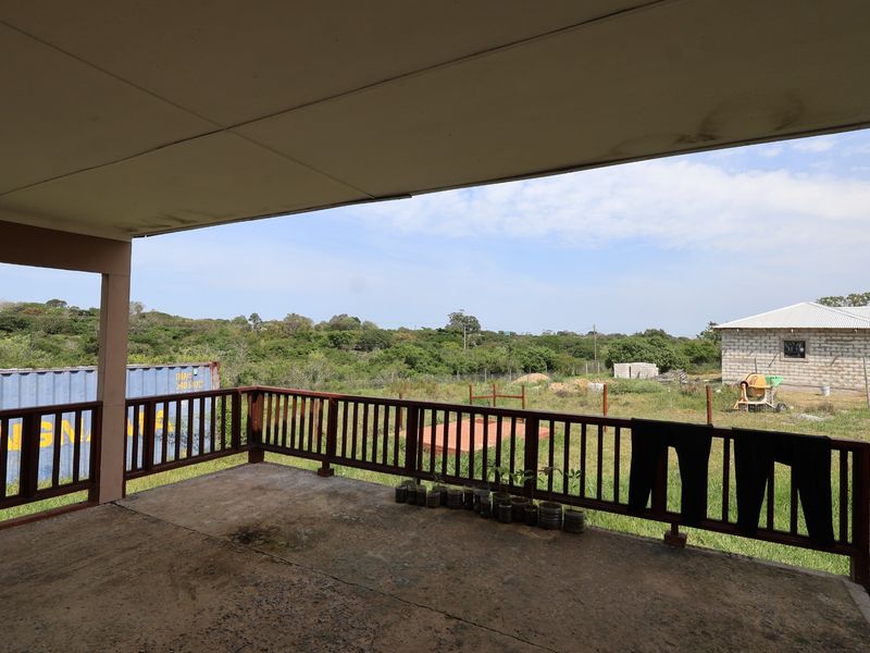 A covered outdoor patio featuring a timber balustrade and concrete flooring, overlooking a rural landscape with surrounding property structures.