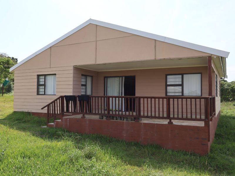Rear view of the house featuring a raised timber deck with balustrade, sliding glass doors, and aluminium window frames set in a grassy yard.