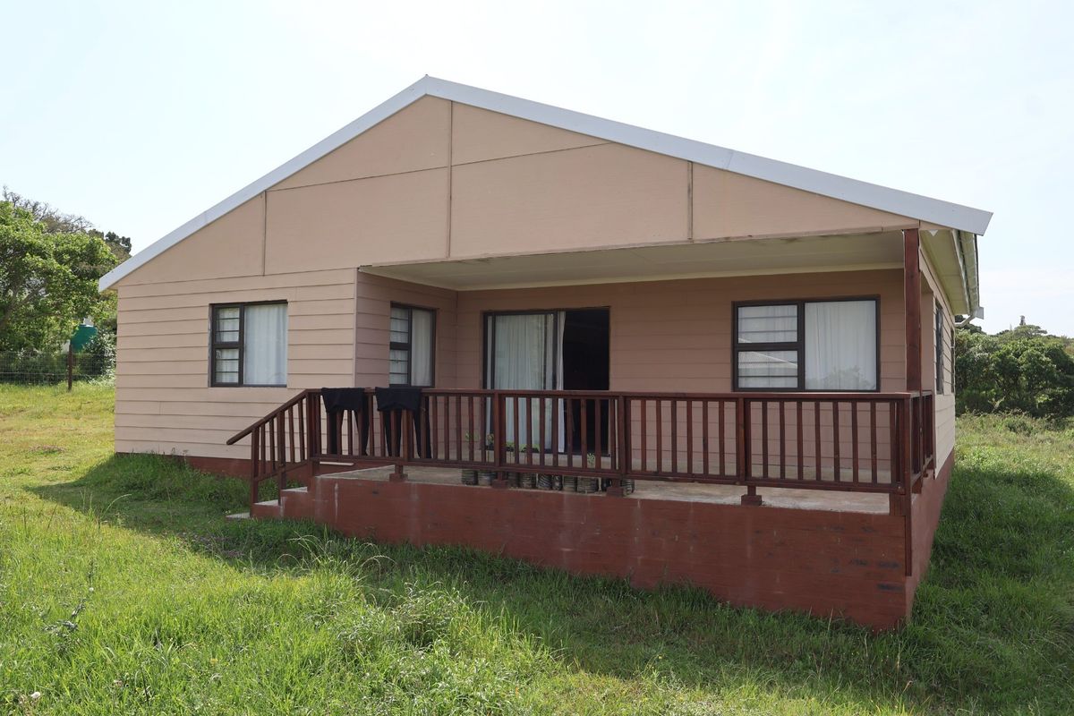 Rear view of the house featuring a raised timber deck with balustrade, sliding glass doors, and aluminium window frames set in a grassy yard.