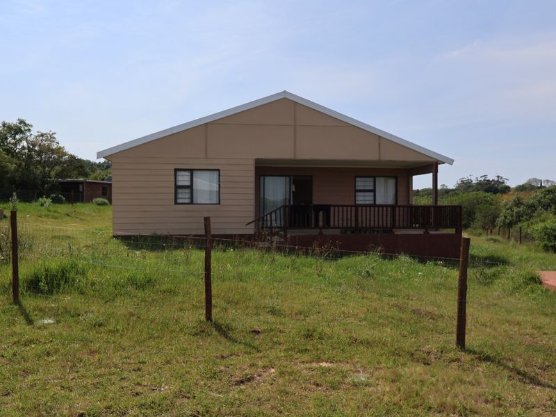 Rear view of a single-story house featuring a timber deck, sliding glass doors, and aluminum window frames set within a large grassy plot.
