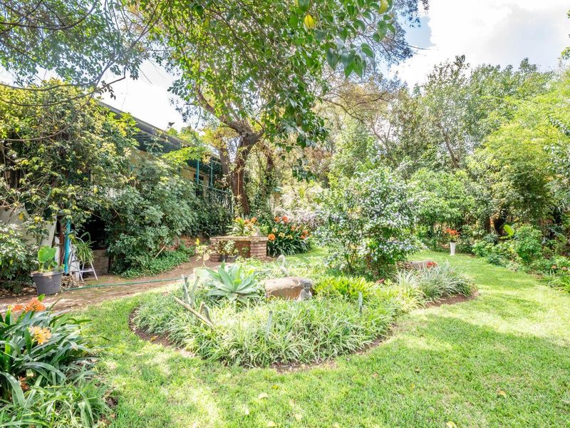 A lush, well-established garden featuring mature trees, manicured lawn areas, and a brick pathway leading alongside the property.