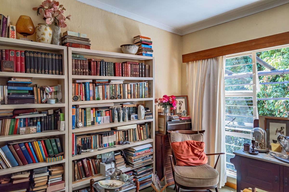 A bedroom featuring built-in floor-to-ceiling shelving and louvered windows with timber trim, offering natural light and garden views.